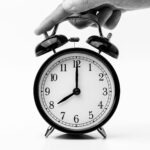 A classic black and white alarm clock being held by a hand, depicting the concept of time.