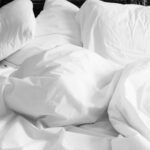 A cozy, rumpled white bed with soft sheets and pillows in a modern bedroom setting.